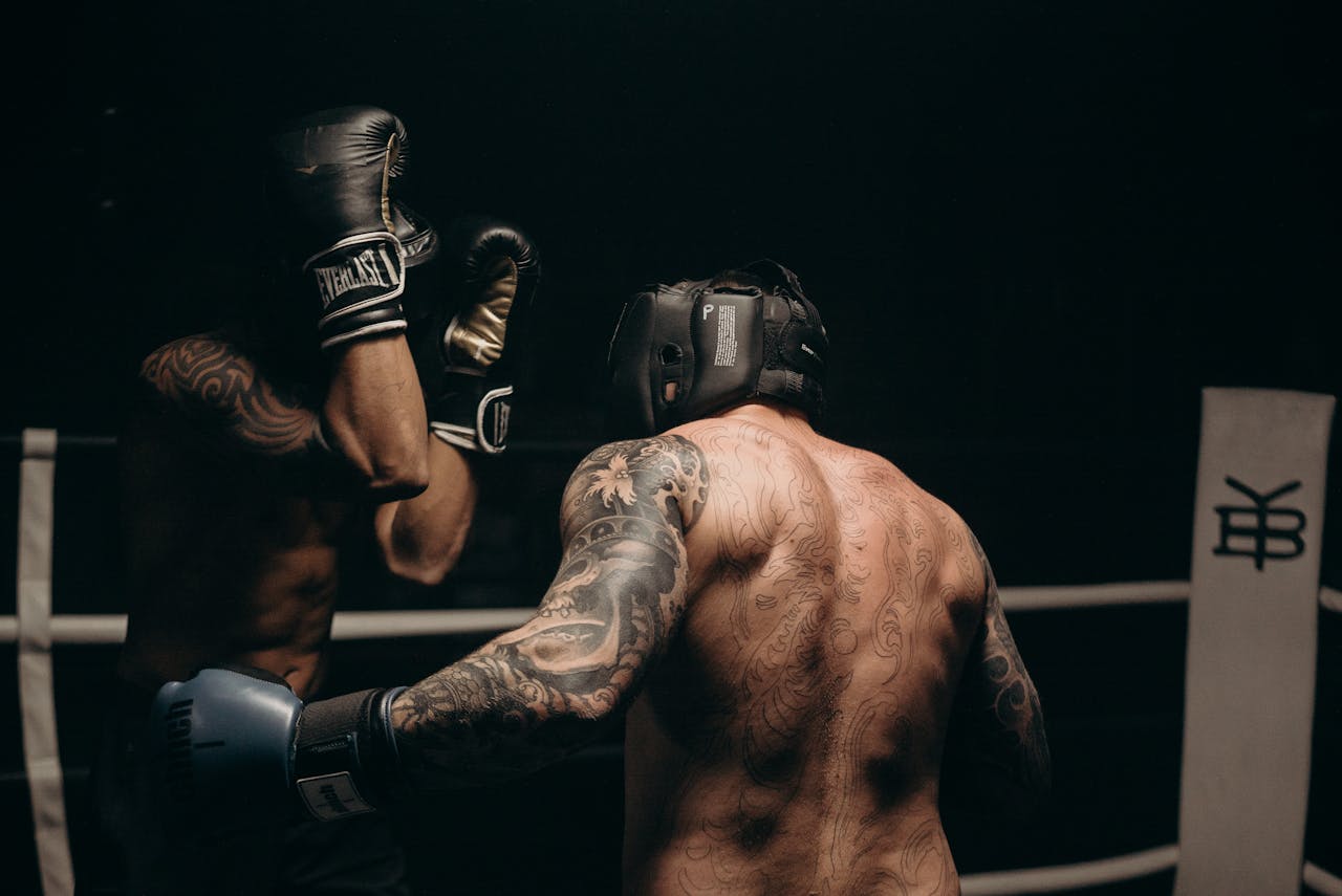 Two tattooed boxers sparring in a dimly lit gym, showcasing skill and strength.